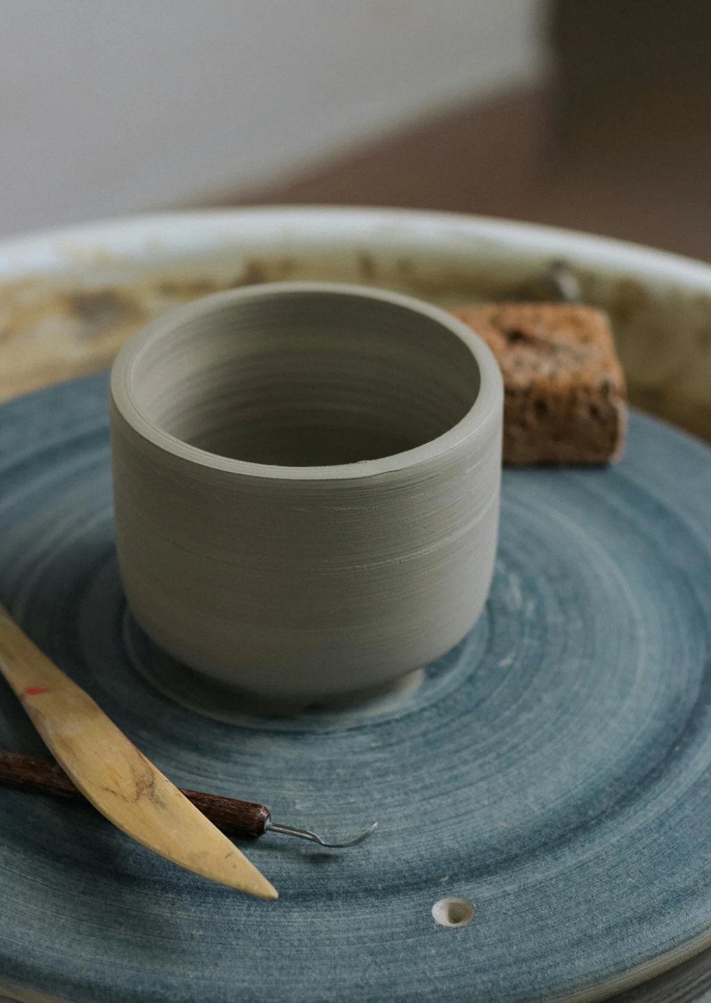 A small thrown vessel on a pottery wheel with two carving tools