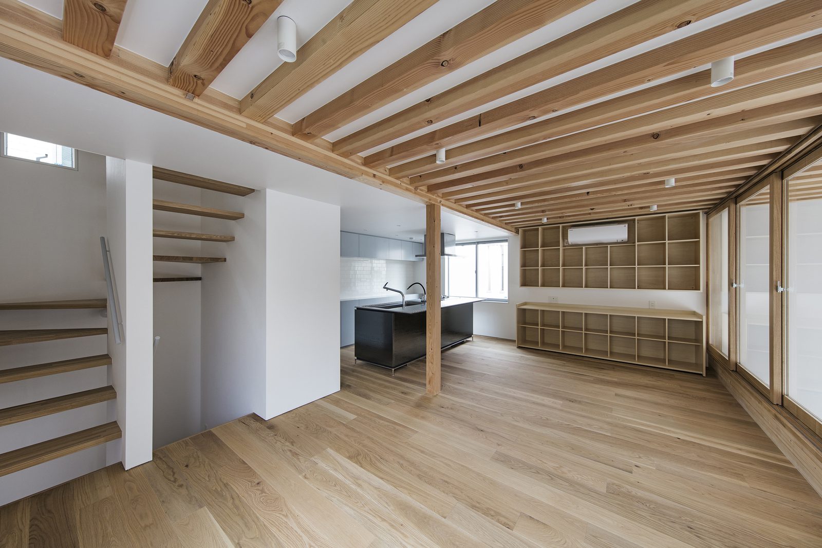 A timber-framed open room with built-in cabinetry and a stair